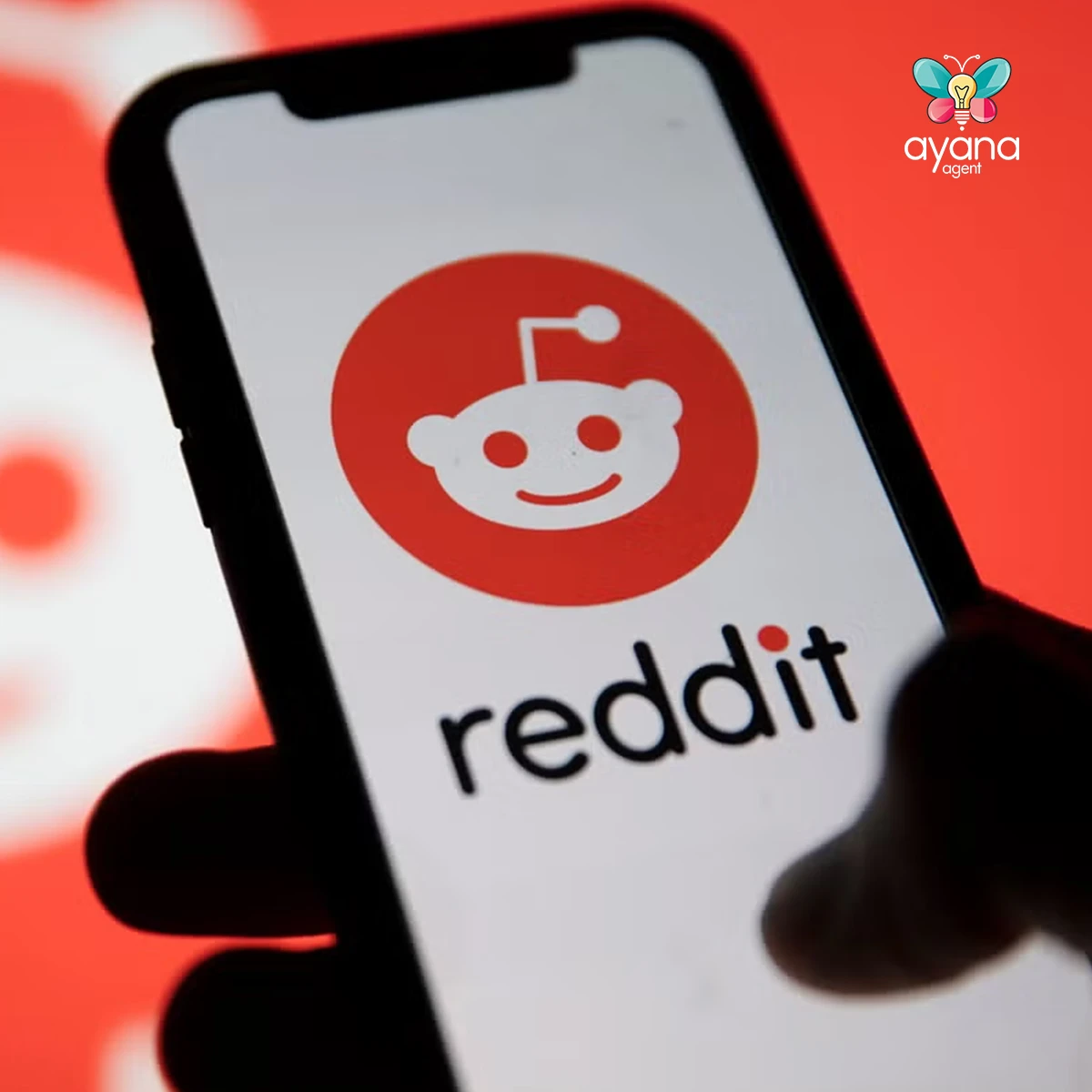 Close-up photo of a phone showing the Reddit logo, held against a red background